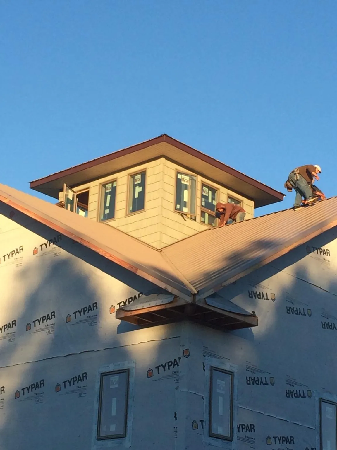 Roofers working around a rooftop cupola on a new metal roof at sunset in Clinton